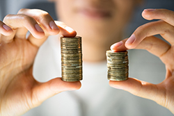 two hands holding uneven stacks of coins